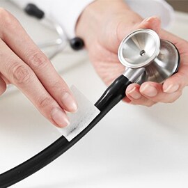 Hands wiping down the tubing of a Littmann stethoscope using an alcohol wipe.