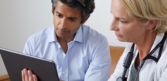 A doctor with a stethoscope around her neck, and a patient, looking at a tablet.
