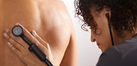 A doctor holding a 3M™ Littmann® CORE Digital Stethoscope up to a patient's back.
