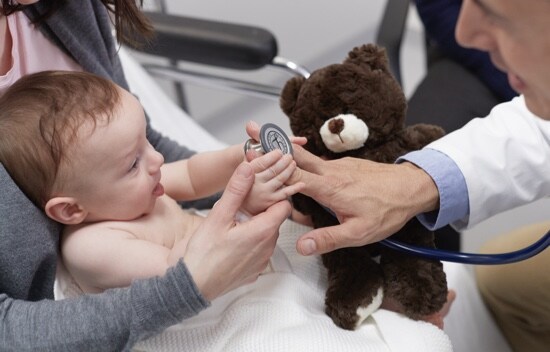 Médecin montrant son stéthoscope à un bébé tenu par sa mère.