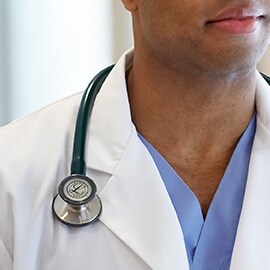 Littmann stethoscope properly worn outside the collar of a white lab coat preventing the tubing from touching the clinician’s neck.