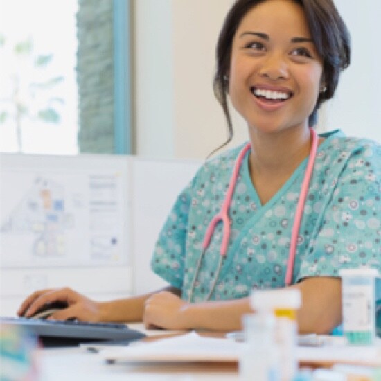 A smiling nurse with a pink stethoscope around her neck, using a computer.